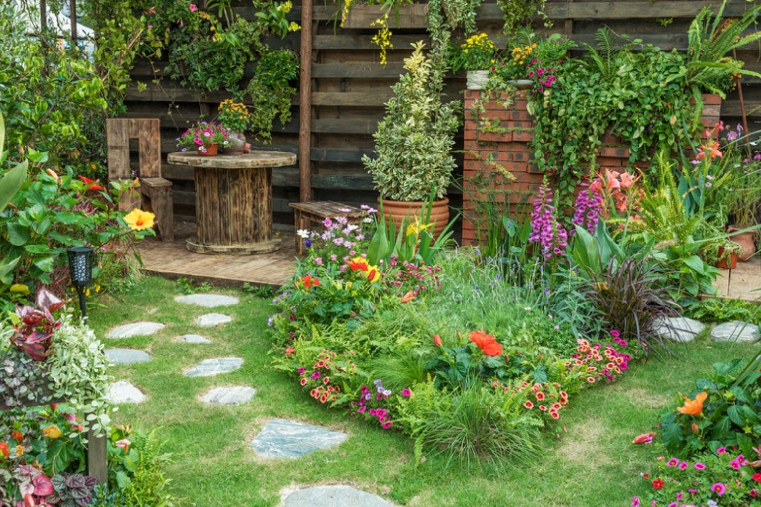 Baghave med blomsterbede, stenfliser og frodige planter